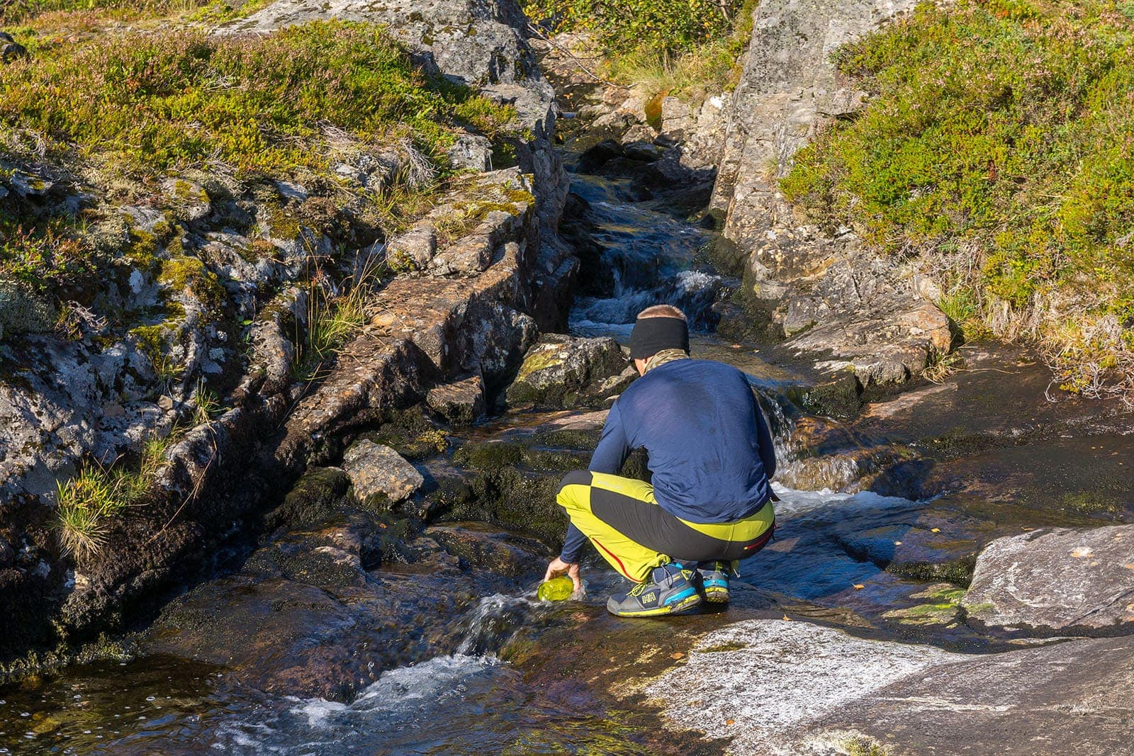 Mężczyzna, wędrowiec, nabierający wodę ze strumienia w górach