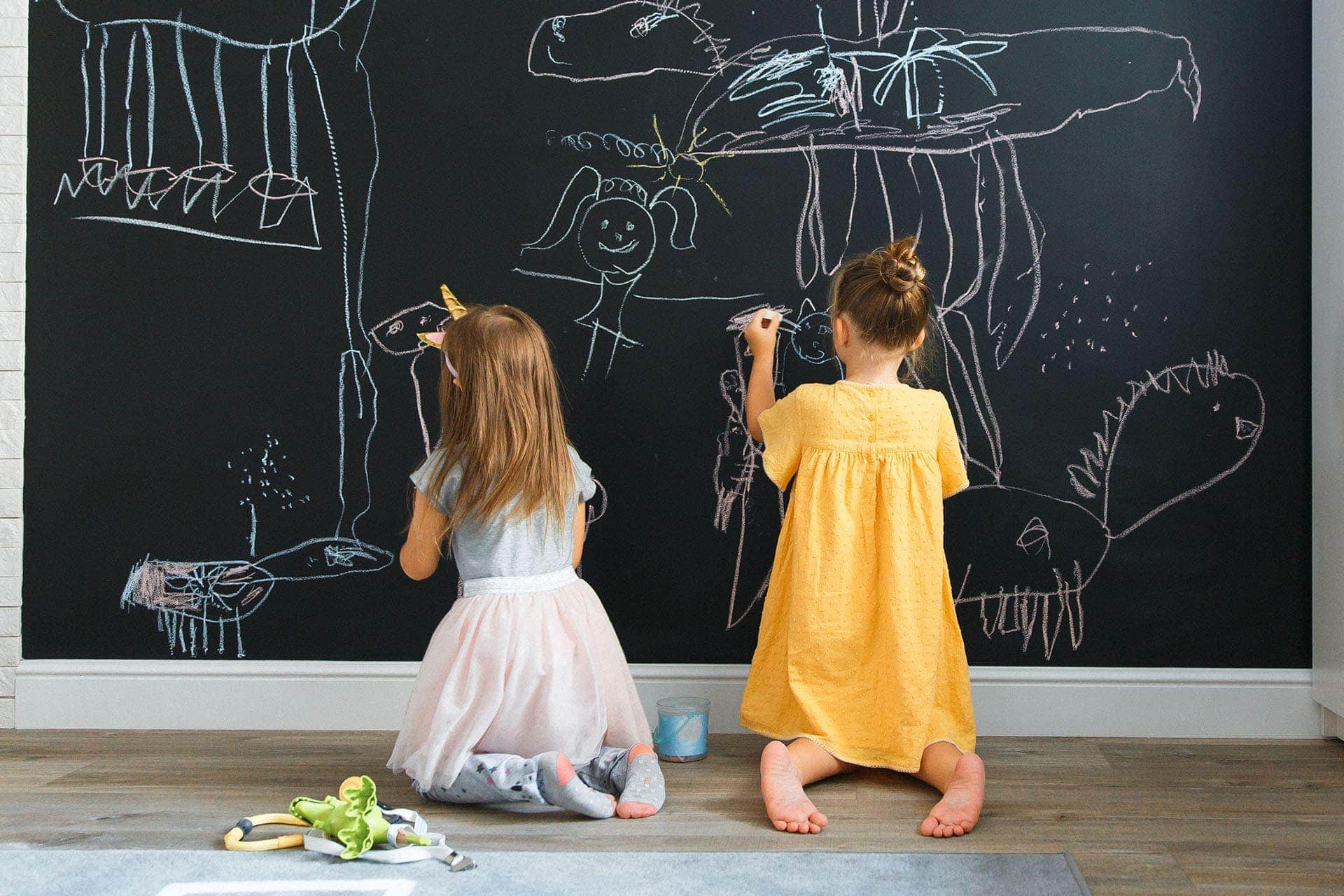 Dwie dziewczynki rysujące kredą na ścianie tablicowej